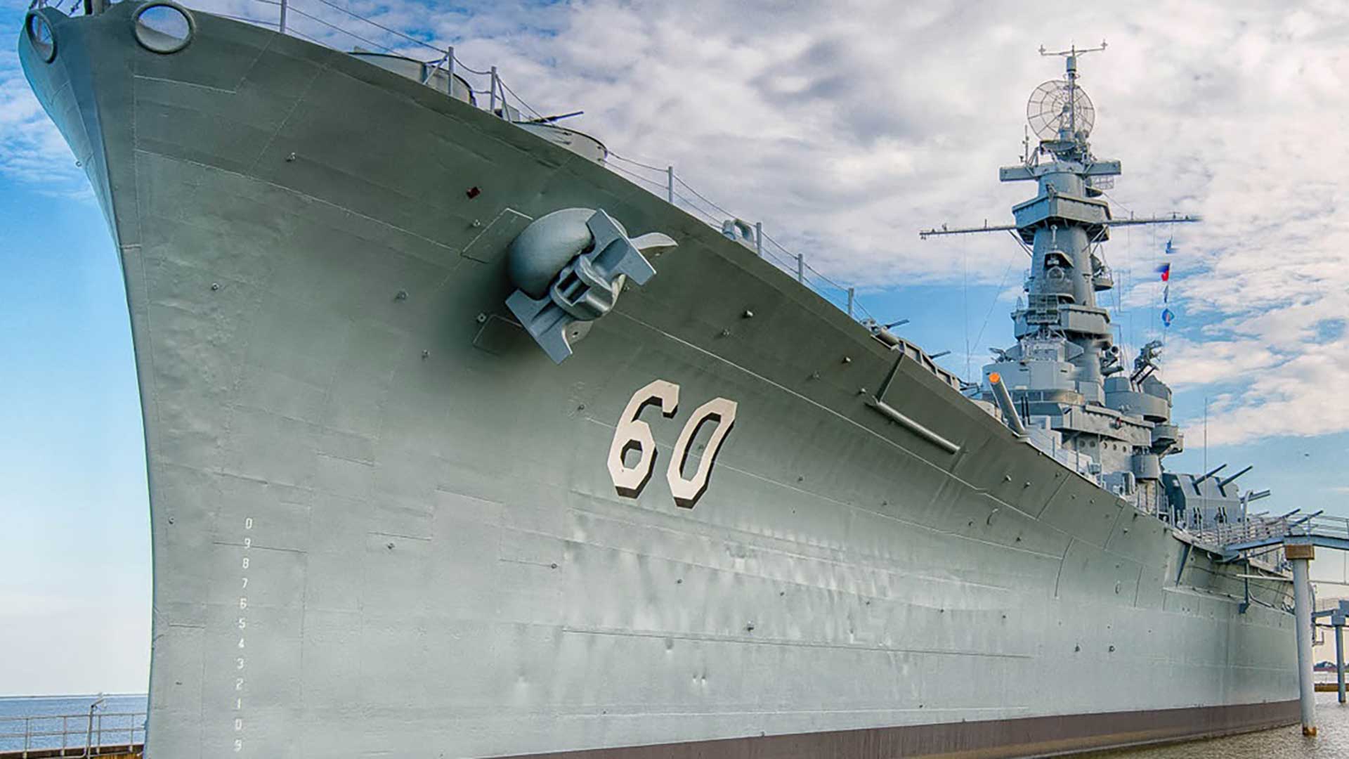 Exterior view of the USS Alabama battleship at Battleship Memorial Park showing the ship’s steel hull, bow number 60, anchor, and superstructure.