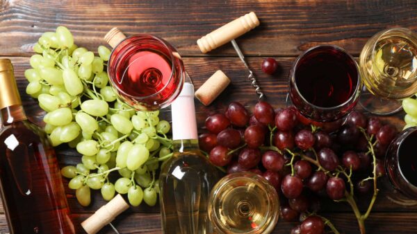 Glasses of wine and wine bottles on a tray with green and red grapes.