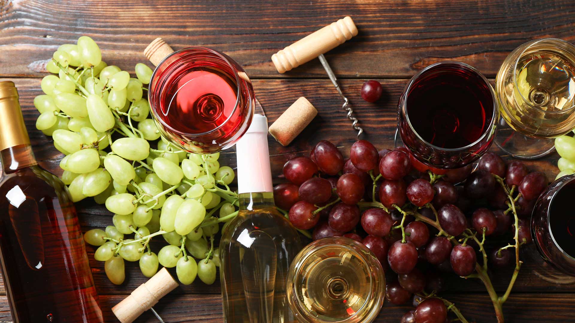 Glasses of wine and wine bottles on a tray with green and red grapes.