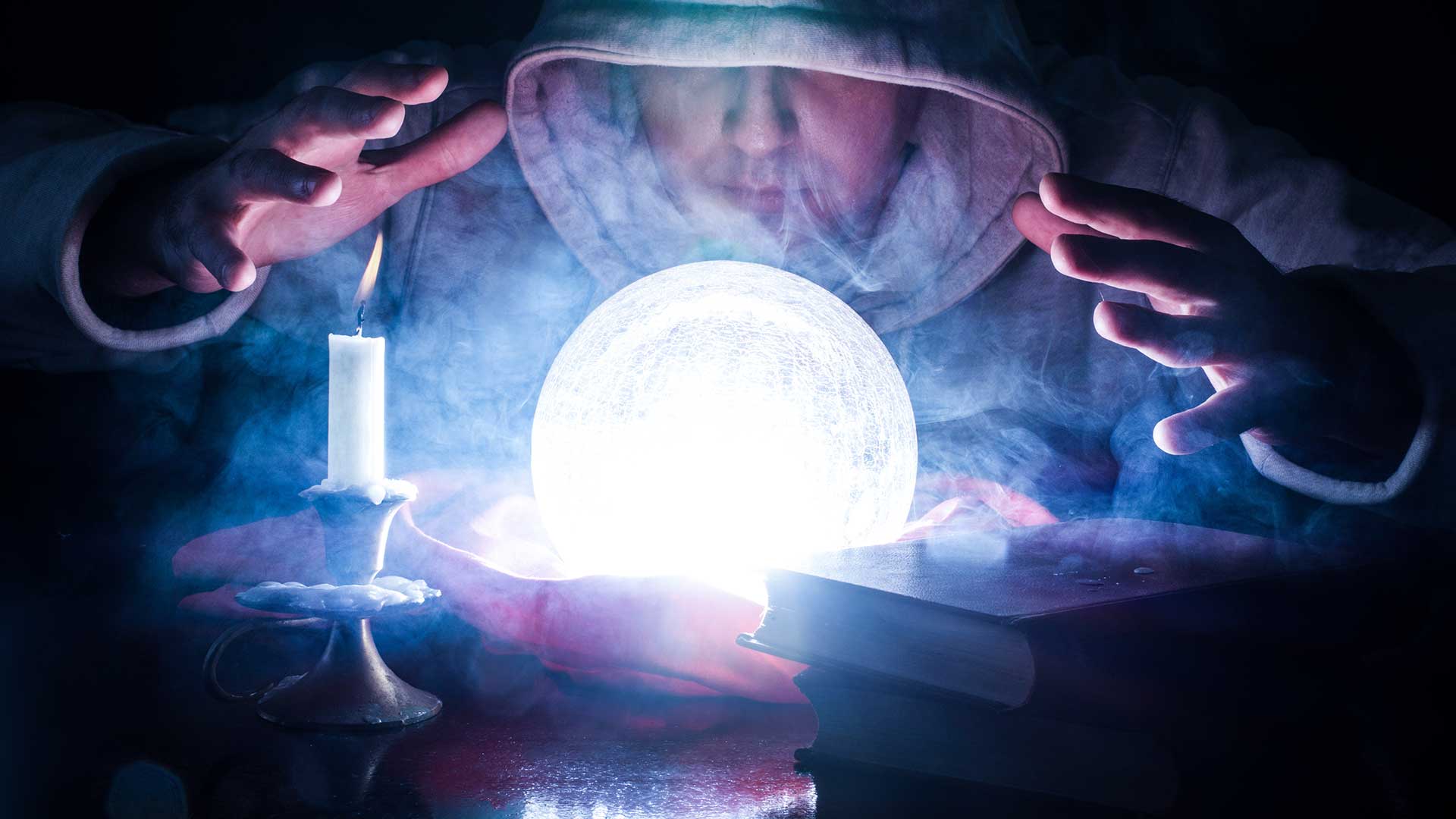 A hooded figure gazes into a glowing crystal ball surrounded by smoke, with a lit candle and books nearby.