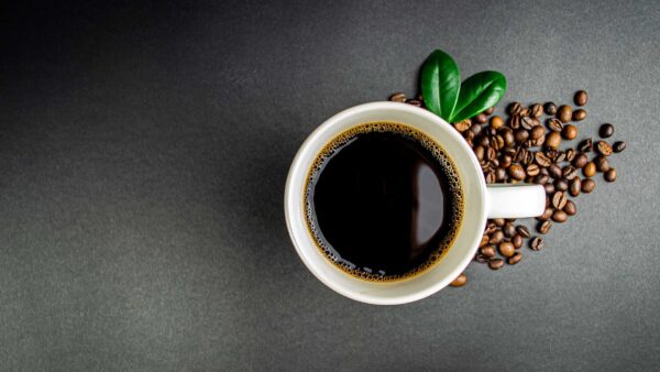 Cup of black coffee surrounded by roasted coffee beans on a dark surface.