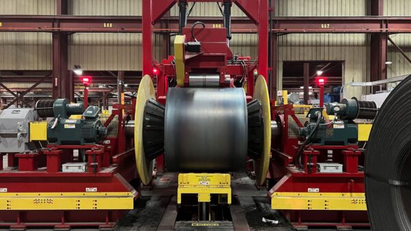 Large steel coil positioned in a red and yellow industrial cut-to-length line inside a manufacturing facility.