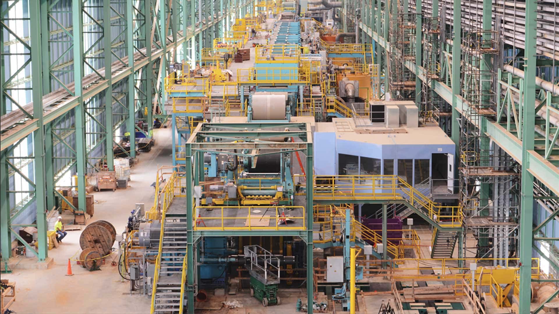 Interior view of a large industrial steel manufacturing facility featuring automated production equipment, processing lines, elevated platforms, and material handling systems.